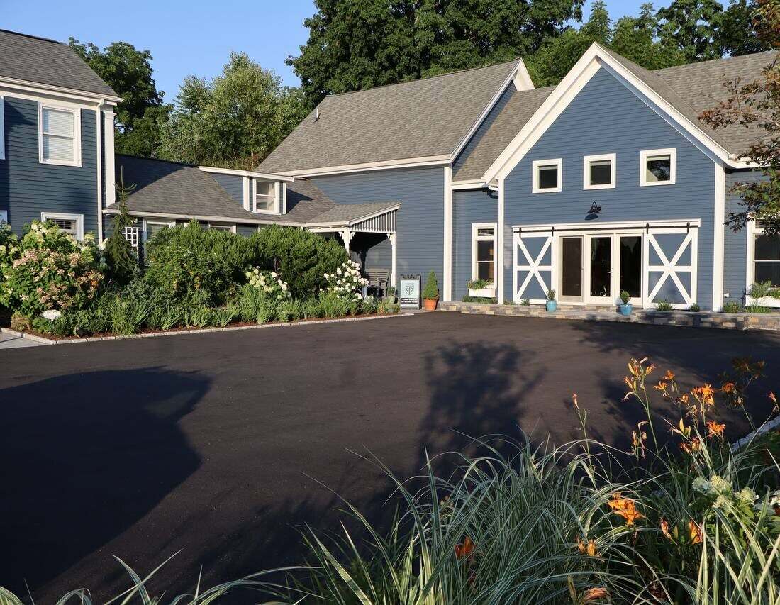 The blue barn-style clinic building at 10 Eliot Street, with gardens, a paved parking area and barn-door entrance